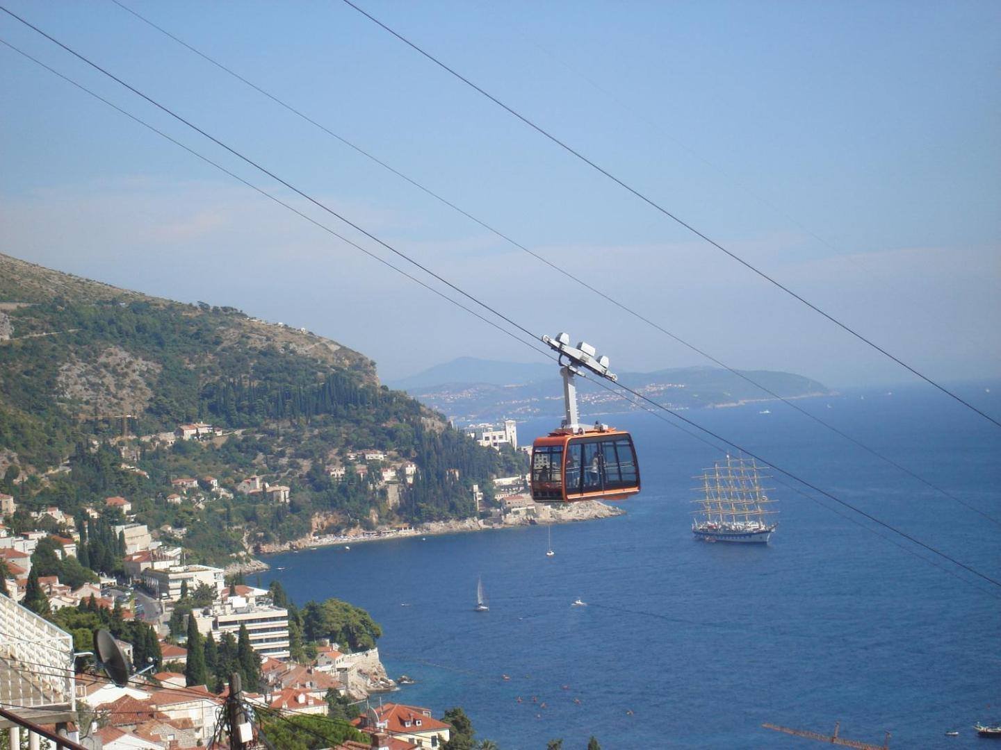 Cable car above the bay with a sailing ship, seen from the apartments